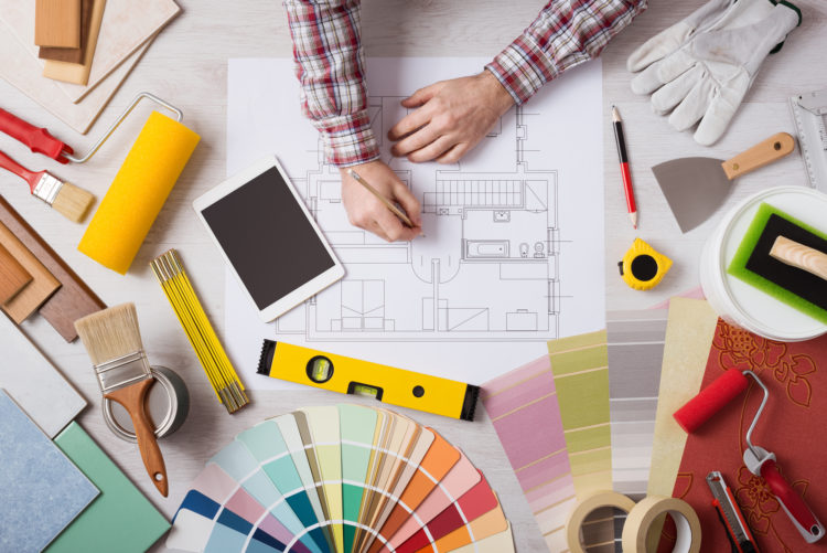 Professional decorator drawing on a house project with work tools, painting rollers and color swatches all around, top view