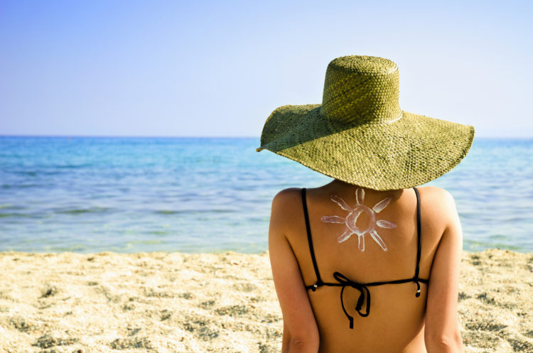 Woman on beach with sun symbol on her back - UV protection concept