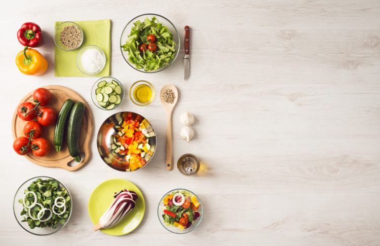 Healthy eating concept with fresh vegetables and salad bowls on kitchen wooden worktop, copy space at right, top view