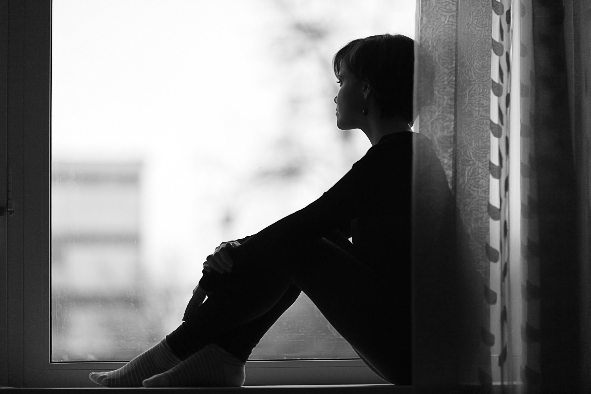 sad girl on the windowsill looking out the window