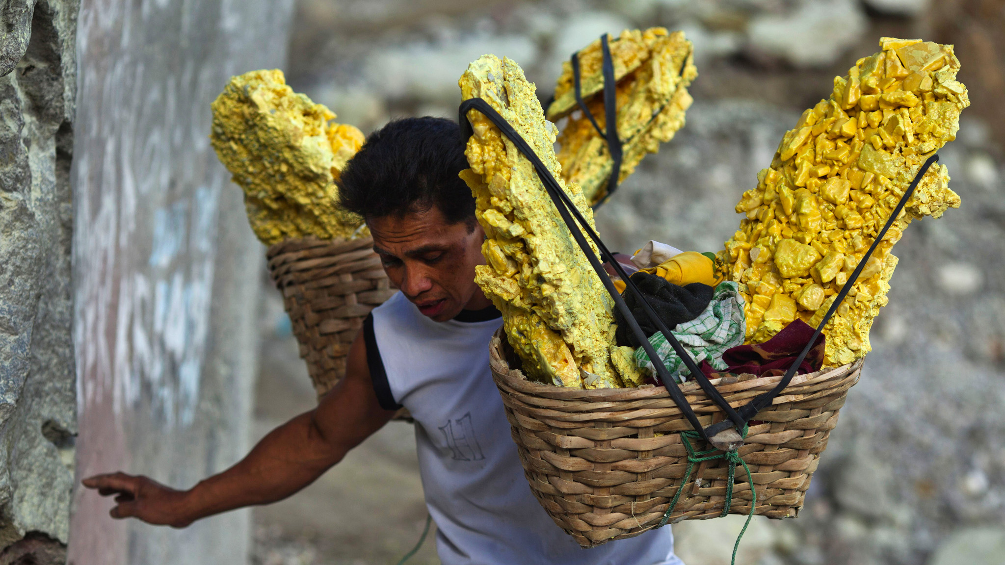 A miner carries baskets of sulphur (sulfur) stones out of the crater at the Kawan Ijen volcano in East Java, Indonesia, on Friday, Aug. 16, 2013. Miners collect sulphur from the active volcano daily to sell to local factories where it is used to refine sugar, make matches and medicines. Photographer: Angel Navarrete/Bloomberg